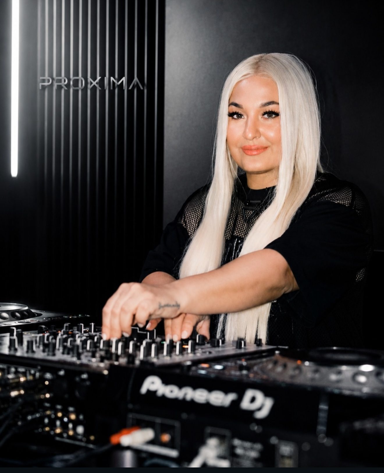 TENAJ playing a Pioneer DJ set-up beneath the Proxima Records sign.